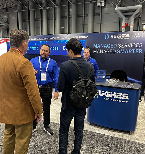 Hughes person talking to two people at a conference 