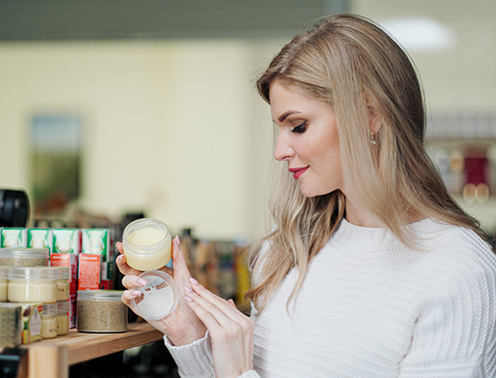 A young blonde woman in a white sweater chooses cream in a cosmetics store. Smearing the cream on hand
