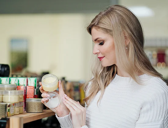 A young blonde woman in a white sweater chooses cream in a cosmetics store. Smearing the cream on hand
