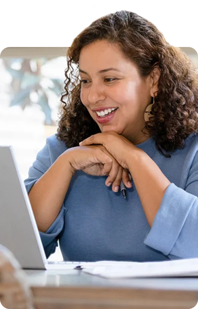 A woman sitting at a table looking at her laptop.